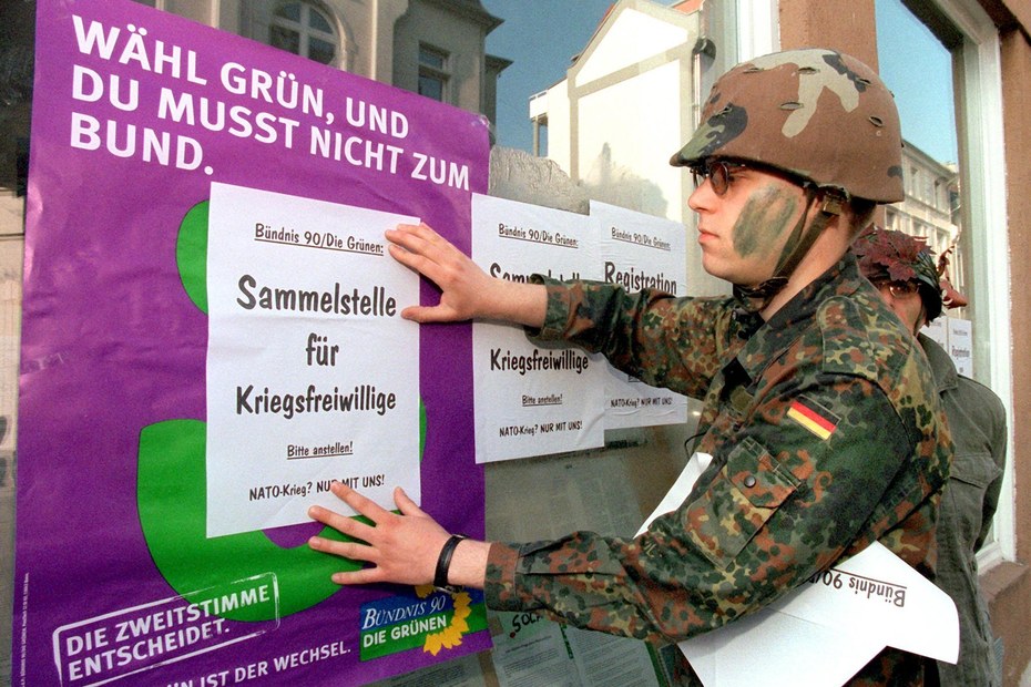 Ende April 1999, Darmstadt: Ein als Soldat verkleideter Friedensaktivist aktualisiert ein Wahlplakat der Grünen