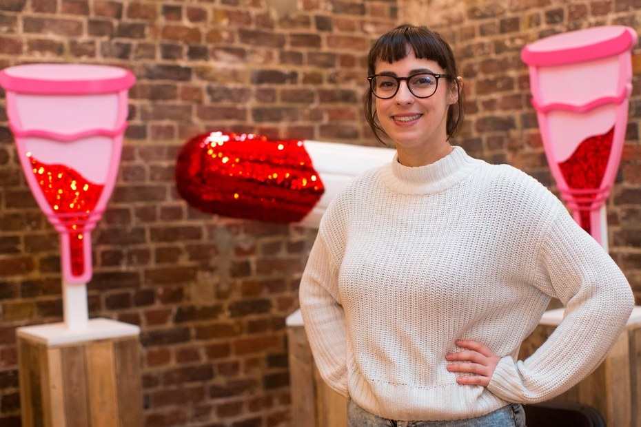 Direktorin des „Vagina Museum“ Florence Schechter vor rot glitzernden Menstruationstassen und Tampons