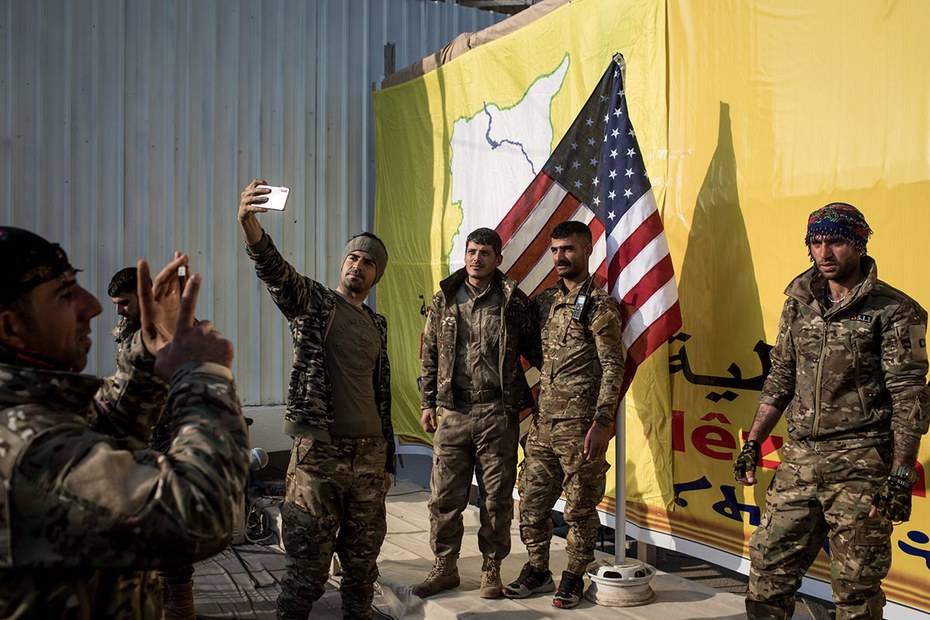 Kämpfer der Demokratischen Kräfte Syriens posieren vor einer amerikanischen Flagge bei einer Veranstaltung anlässlich des Sieges über den IS im März 2019