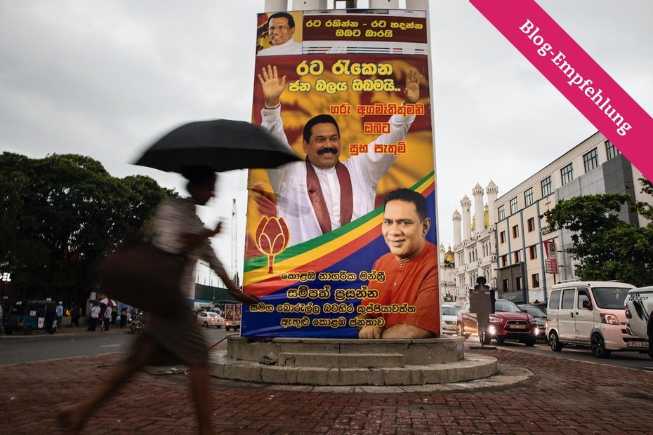 Eine Frau vor einem Plakat, welches den aktuellen Premierminister Mahinda Rajapaksa zeigt