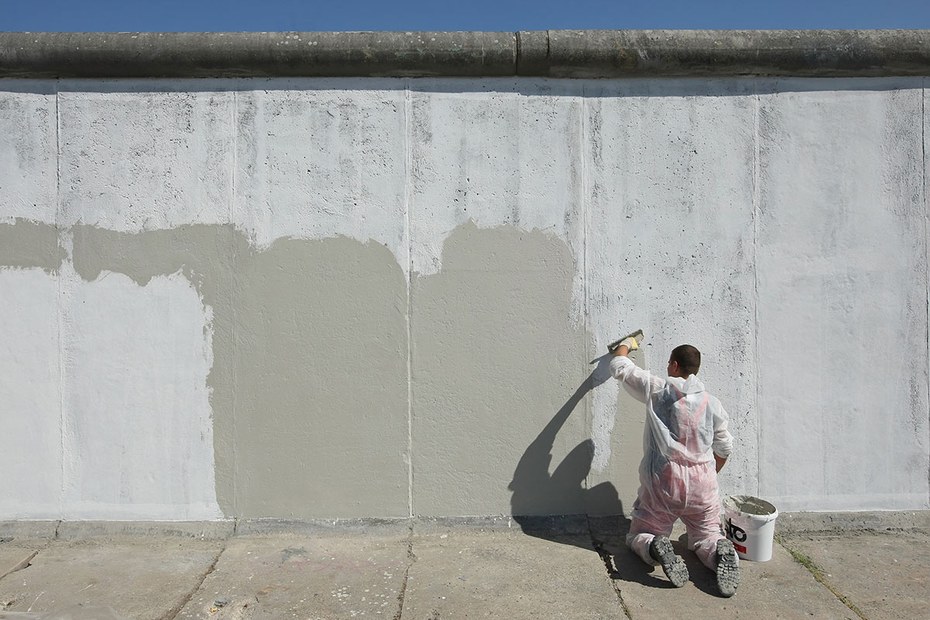 Ein Maler streicht einen Teil der ehemaligen Berliner Mauer