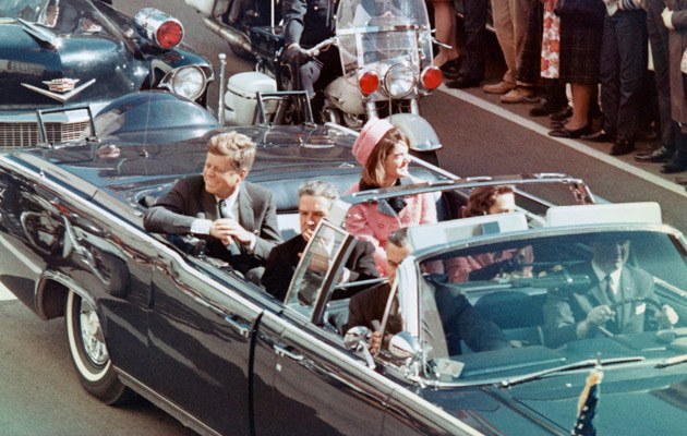John F. Kennedy und seine Frau Jackie lächeln am 22. November 1963 hinüber zur Menge - Minuten später wird der Präsident erschossen
