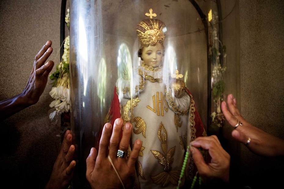 Hände greifen nach einer Figur der heiligen Maria, Mutter Gottes, die in einer Kirche in Manila steht
