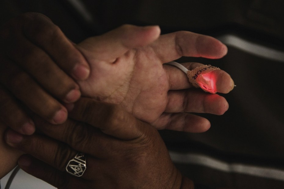 Einem Intensivpflegepatient werden auf der Intensivstation von seinem Vater die Hände massiert