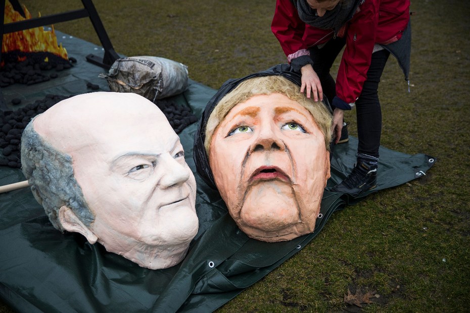 Eine Umweltaktivistin präpariert Masken mit dem Bild von Bundeskanzlerin Angela Merkel (R) und Bundesfinanzminister und Vizekanzler Olaf Scholz vor dem Reichstagsgebäude