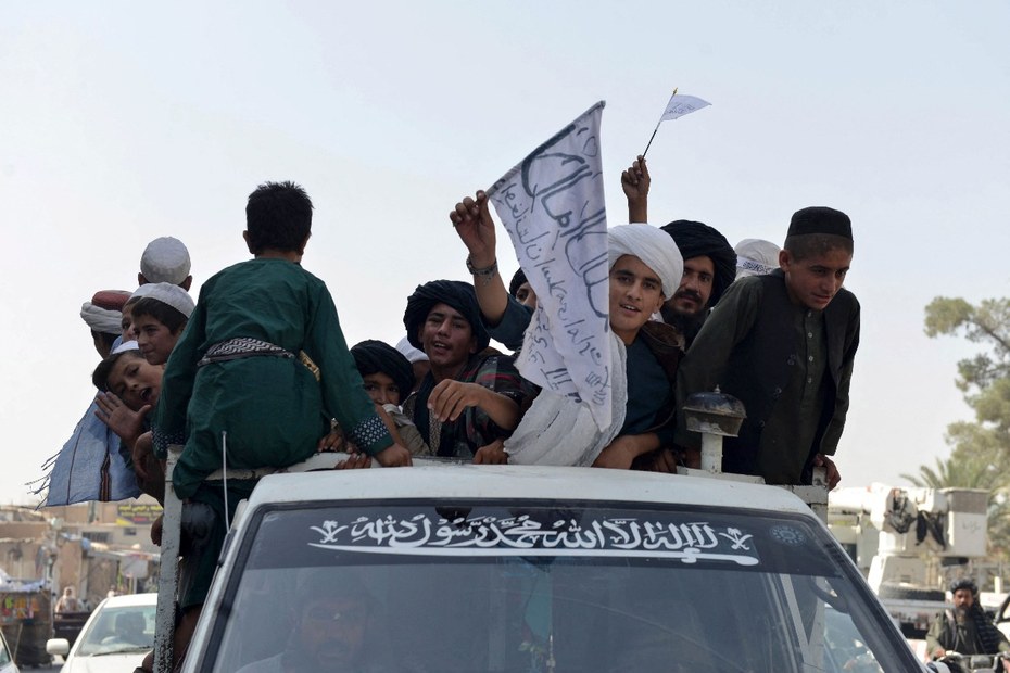 Jugendliche, die die Taliban unterstützen, schwenken Taliban-Fahnen auf einem Fahrzeug, während sie am 31. August 2021 eine Straße in Kandahar (Afghanistan) entlang fahren.