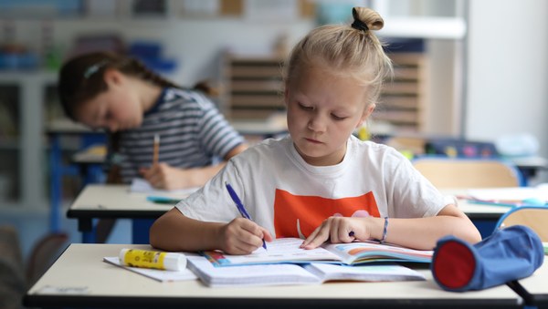 Eine junge Schülerin sitzt an einem Tisch im Klassenraum und schreibt in ihr Heft.
