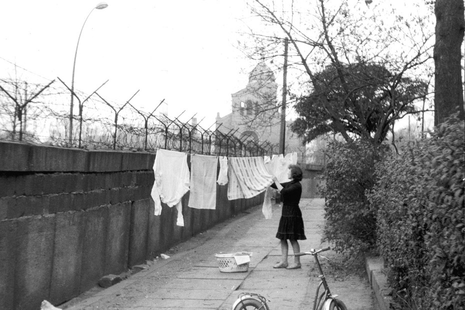 Eine deutsche Frau hängt Kleidung zum Trocknen auf einer Leine auf, die zwischen einem Baum und der Berliner Mauer gespannt ist, 13. November 1963.