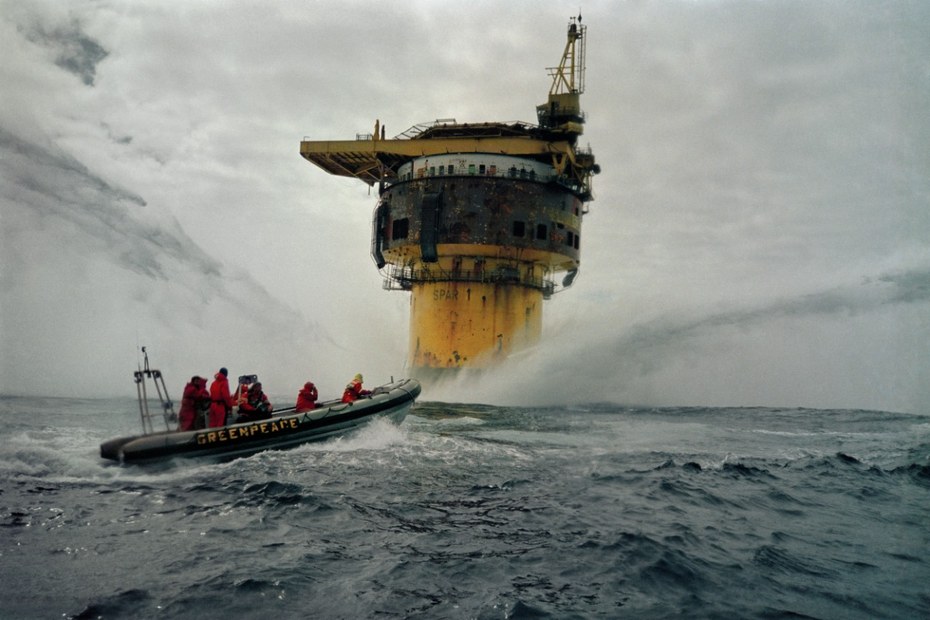 Aktivistinnen und Aktivisten von Greenpeace vor einem Bohrturm im Meer.
