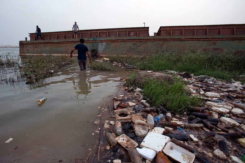 Ein Mann läuft im Fluss Shatt Al-Arab in der Hafenstadt Basra durch Müll, hauptsächlich Plastikmüll.