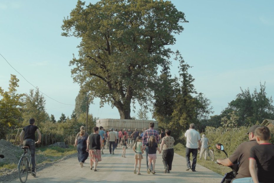 Eine Dorfgemeinschaft begleitet einen soeben entwurzelten Baum auf dem Weg hinaus aus ihrem Dorf. Eine Dorfgemeinschaft begleitet einen soeben entwurzelten Baum auf dem Weg hinaus aus ihrem Dorf.