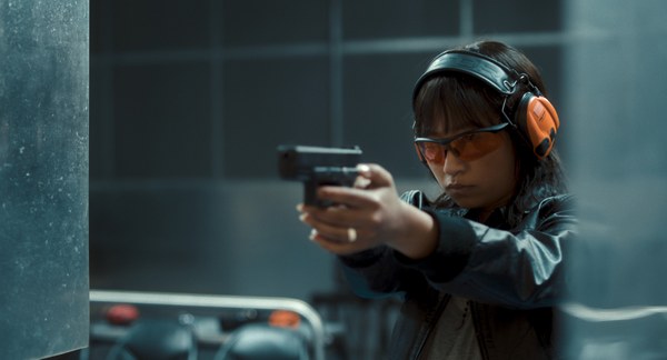 Die Staatsanwältin Seyo Kim steht in einer Schießstätte, sie hat eine Schutzbrille und Schutzkopfhörer auf, eine Pistole in der Hand und übt schießen.